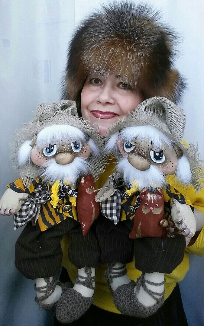 a woman holding two small dolls in her hands and wearing fur hats on top of their heads