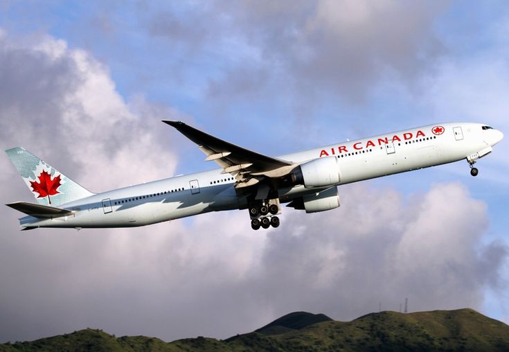 an air canada plane flying in the sky with mountains in the back ground and clouds in the background