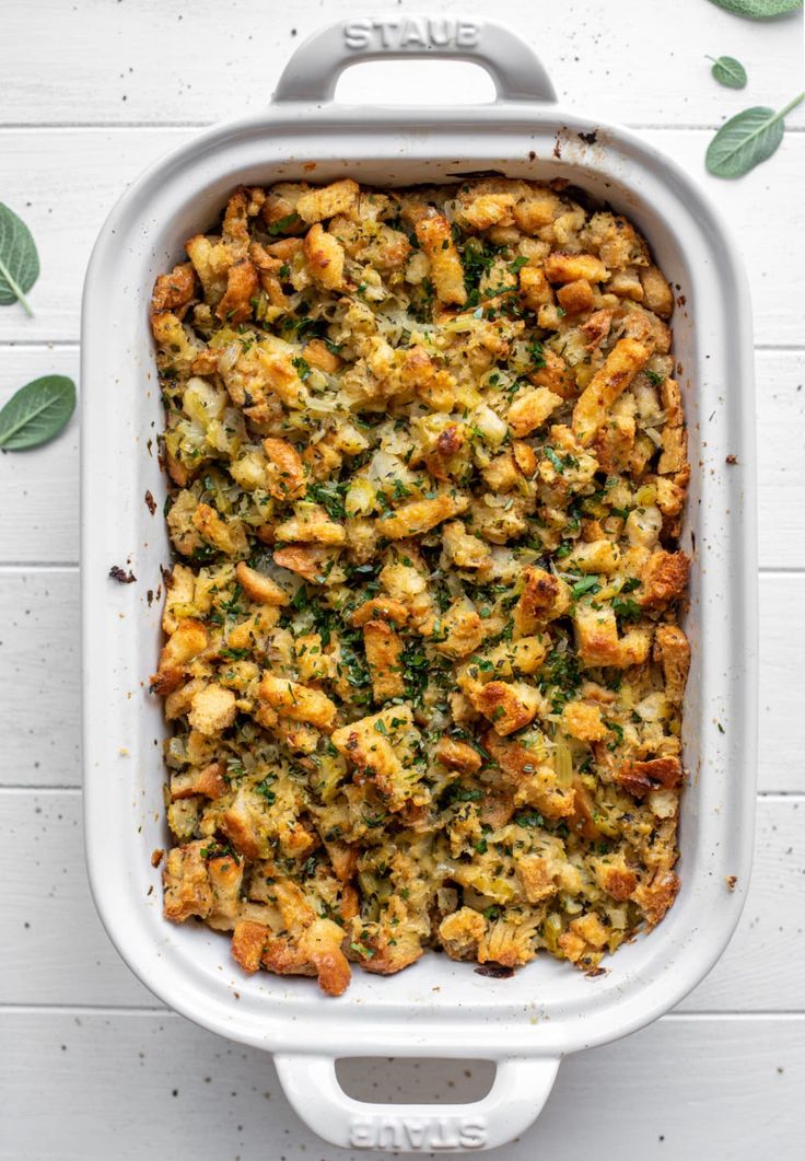 a casserole dish filled with stuffing and vegetables on top of a white table