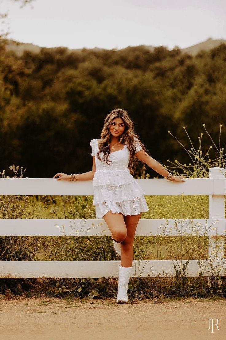 a beautiful young woman posing in front of a white fence