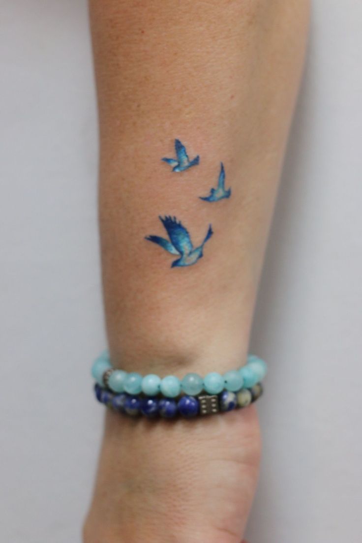 a woman's arm with blue birds on it and beads around her bracelets