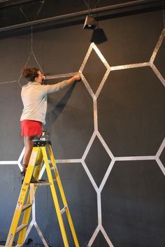 a man on a ladder painting a wall with white hexagonal tiles and a lamp