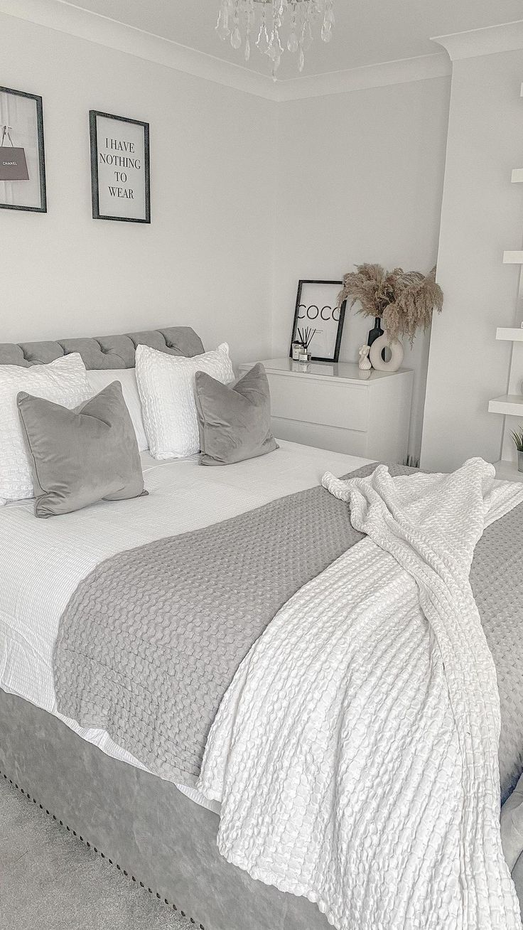 a bed with white sheets and gray pillows in a room that has pictures on the wall