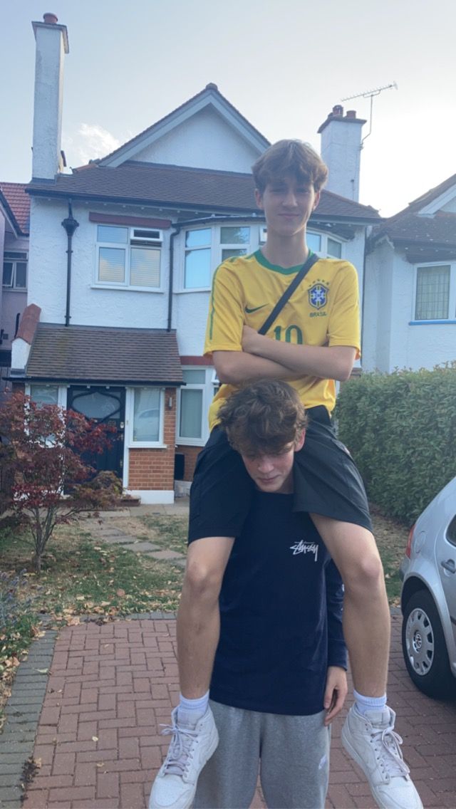 two young men standing on top of each other in front of a house with their arms around one another