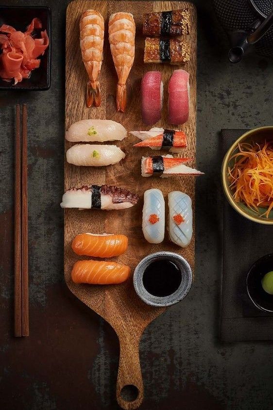 sushi on a cutting board with chopsticks, sauce and other food items