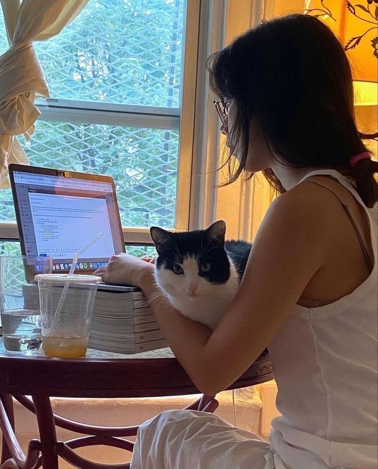 a woman sitting in front of a laptop computer with a black and white cat on her lap