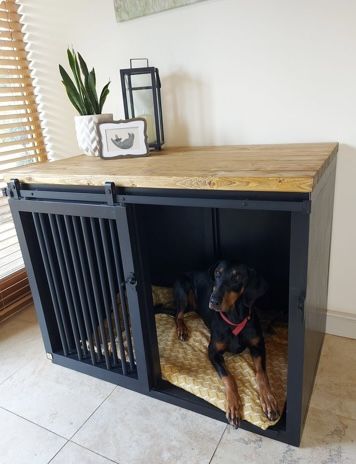 a black and brown dog laying on top of a bed under a wooden table next to a window