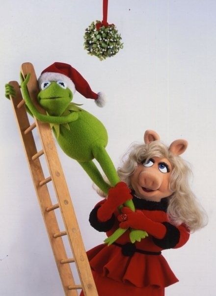 the muppet and miss piggy are hanging from a ladder with christmas decorations in the background