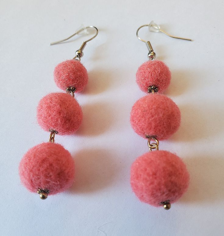 three pink pom - poms hanging from silver earwires on a white surface