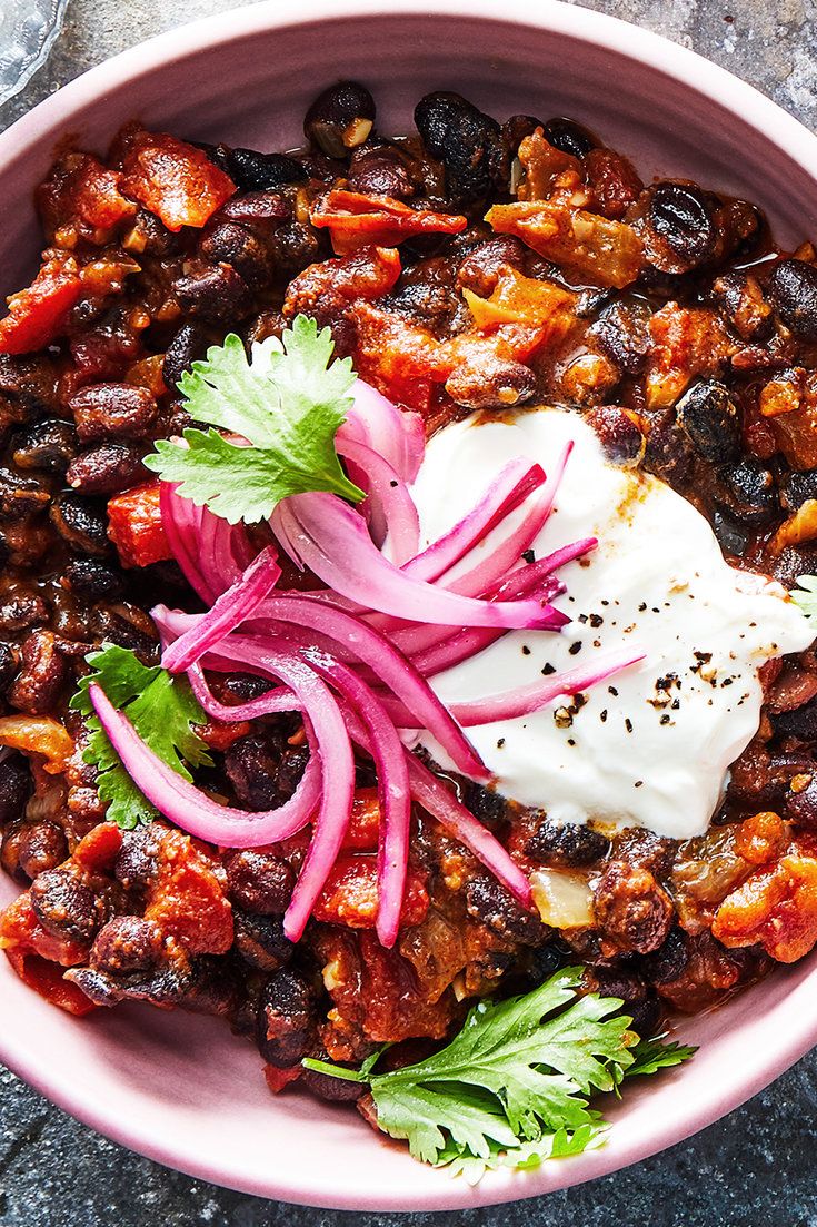 a pink bowl filled with food and garnished with sour cream, onions and cilantro