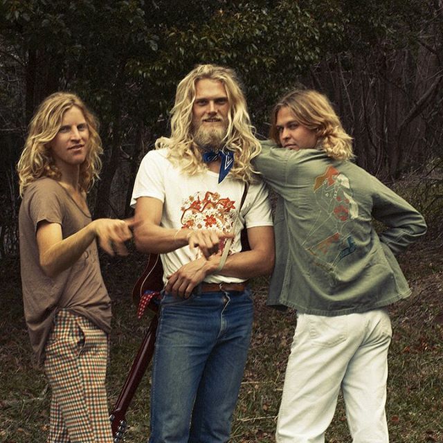 three people standing next to each other in front of trees and grass with one person holding an object