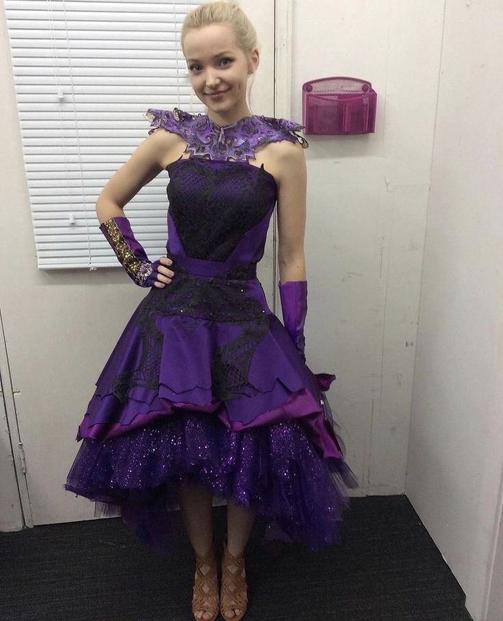 a woman in a purple dress standing next to a door with her hands on her hips