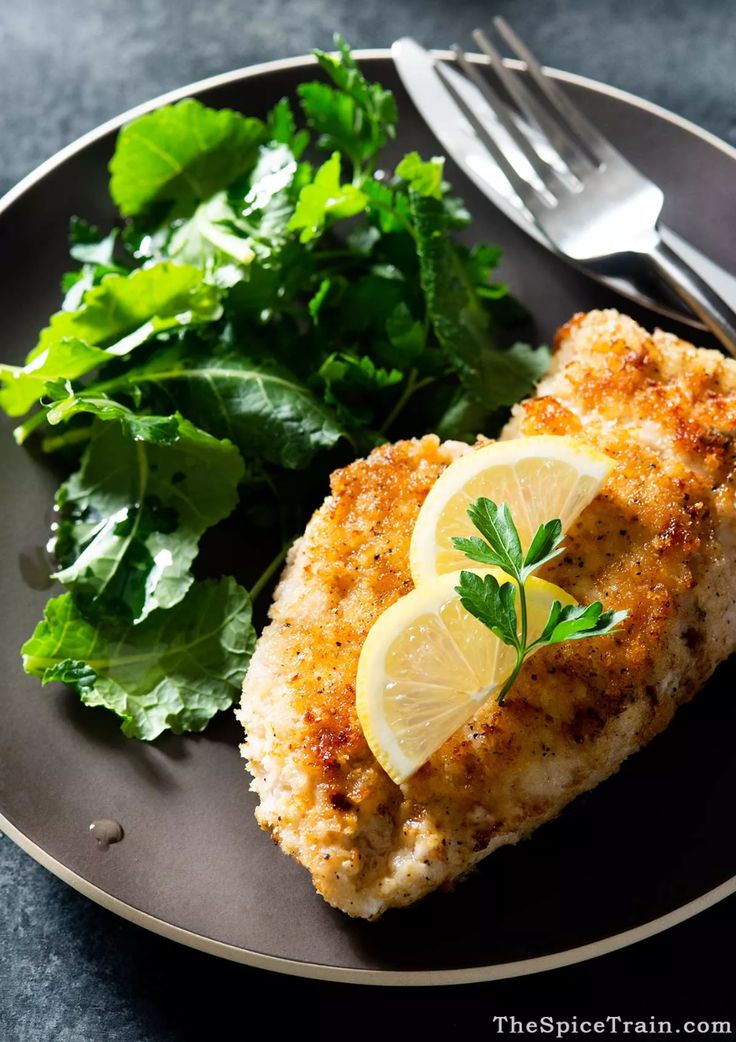 a piece of chicken with lemon and parsley on a plate next to some greens