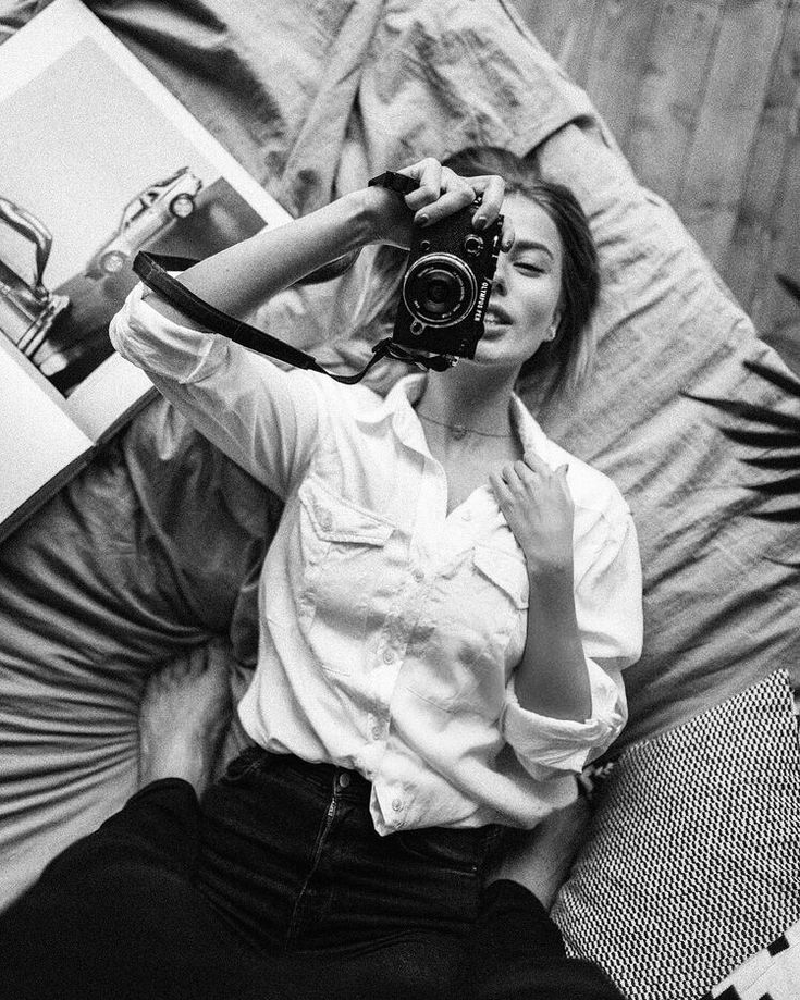 a black and white photo of a woman laying on a bed with a camera in her hand