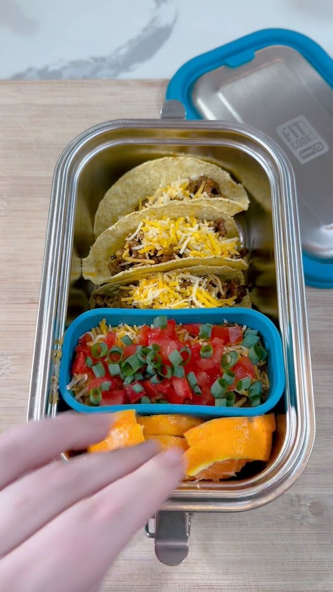 a person is holding their hand out to grab food from a lunchbox with tortillas and peppers