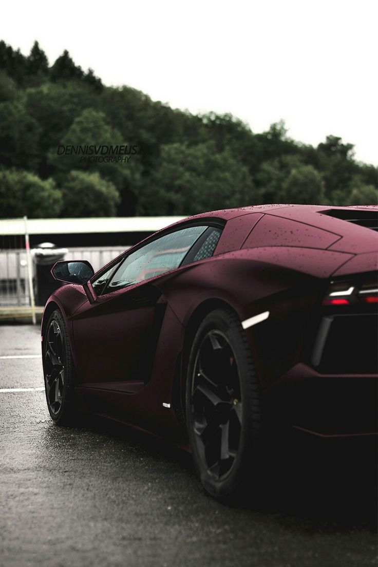 a red sports car parked in a parking lot with trees in the backgroud