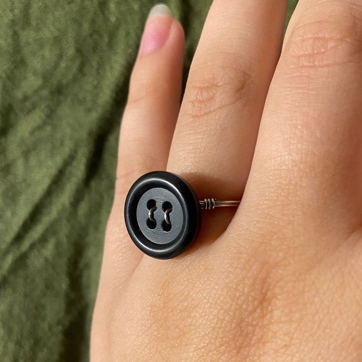 a person's hand with a black button ring on it