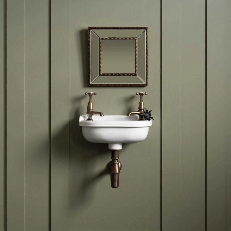 a bathroom sink sitting under a mirror next to a wall mounted faucet