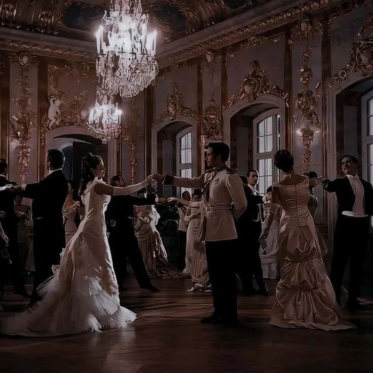 a group of people standing around each other in a room with chandelier and windows