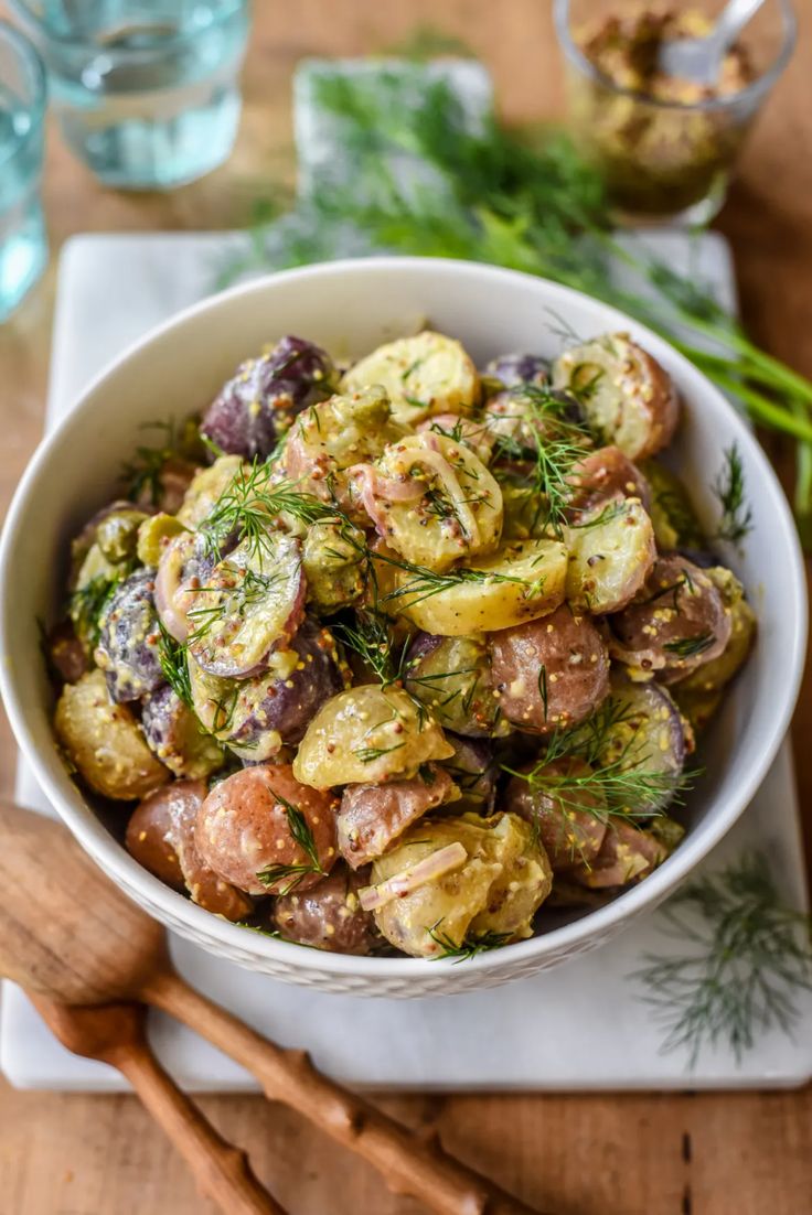 a white bowl filled with potato salad on top of a wooden table next to utensils