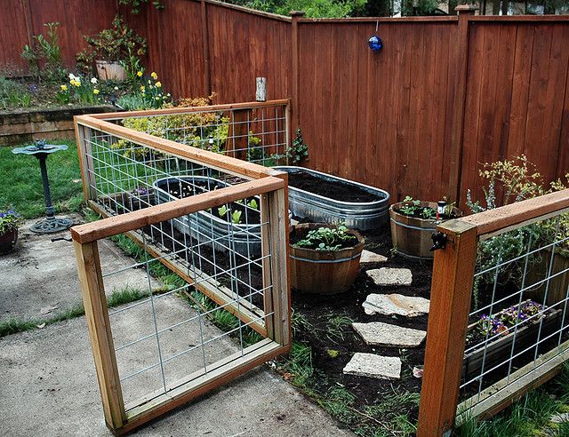 an outdoor garden area with several plants in pots and fenced in areas around it