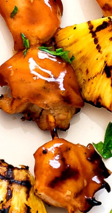 grilled chicken and pineapples on a white plate with green leafy garnish