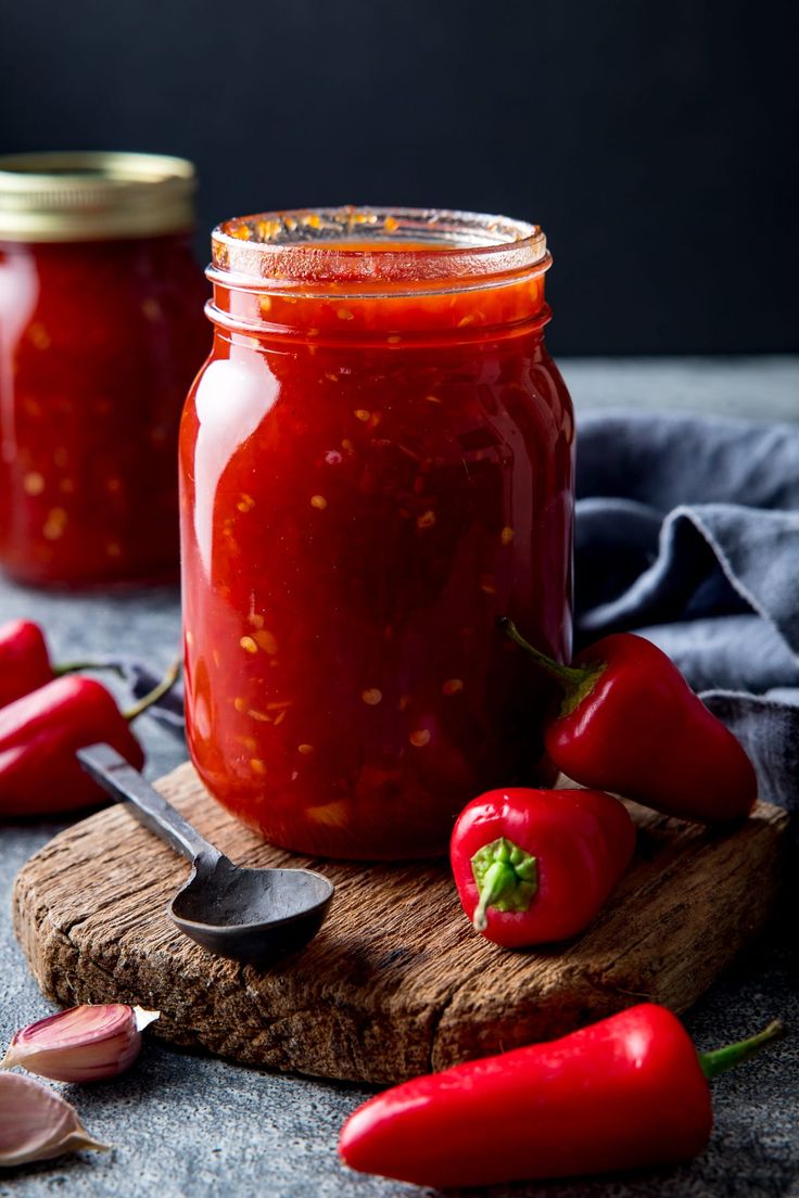 two jars filled with red chili sauce on top of a cutting board next to spoons