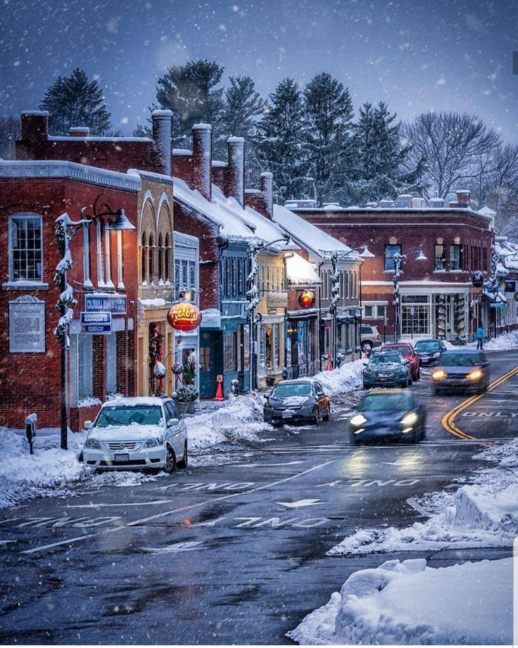 cars driving down a snowy street in the middle of town