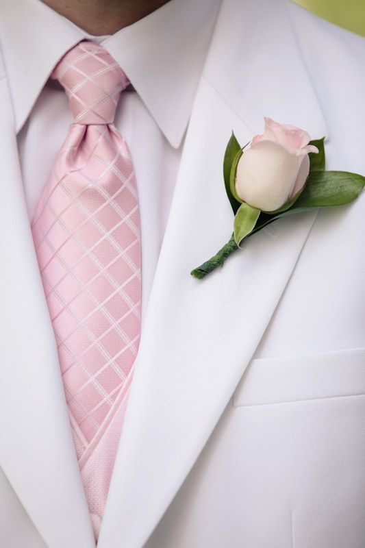 a man in a white suit and pink tie with a rose boutonniere