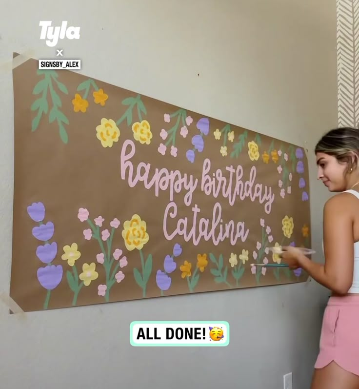 a woman is painting a sign with flowers on it that says happy birthday, claudia