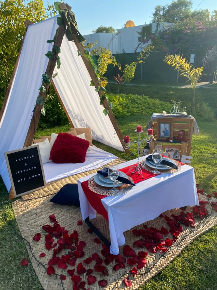 a table set up with red and white petals on the grass