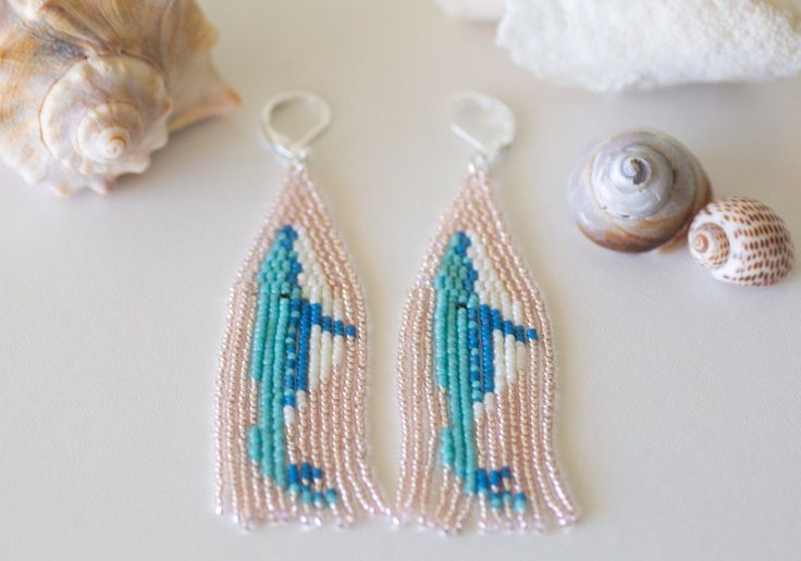 two beaded earrings sitting on top of a table next to seashells