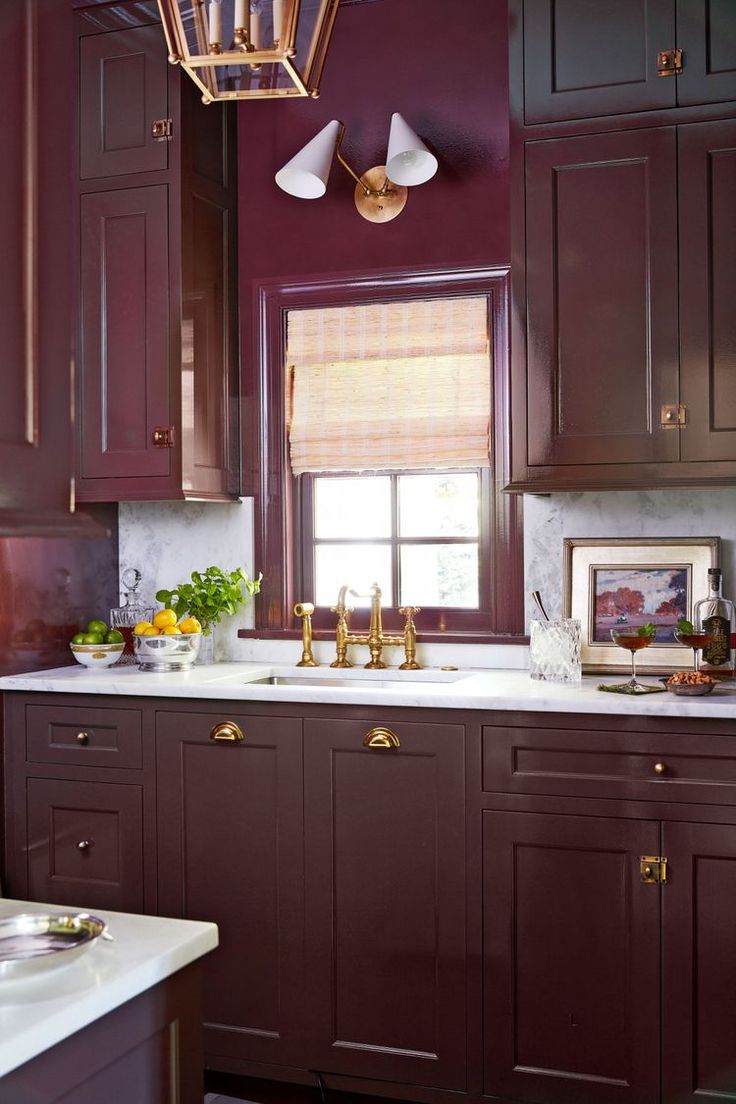 a kitchen with purple cabinets and white counter tops, gold accents on the light fixture