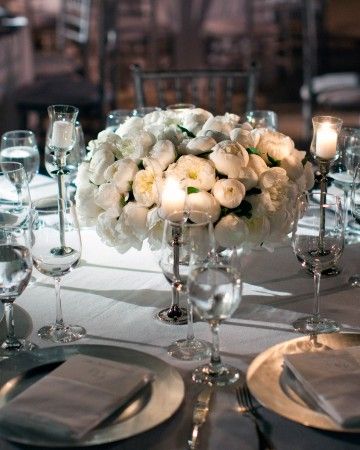 a centerpiece with white flowers and candles is displayed on a table set for an elegant dinner