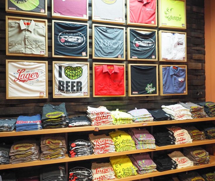 shirts are on display in a store with wooden shelves filled with t - shirts and other items