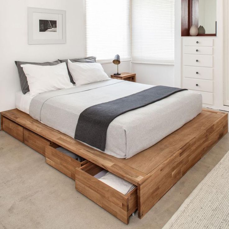 a bed sitting on top of a wooden platform next to a white dresser and window