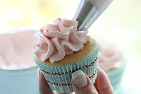 a cupcake with pink frosting being held by a woman's hand,