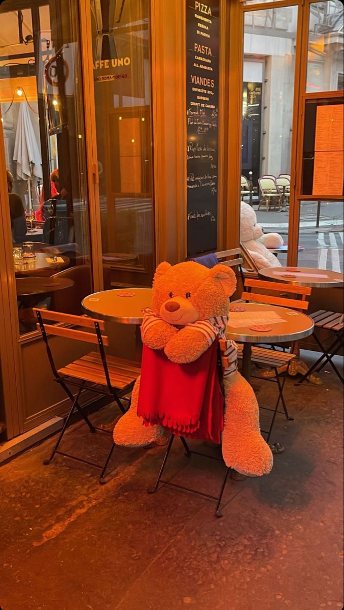 a large teddy bear sitting on top of a chair in front of a restaurant window