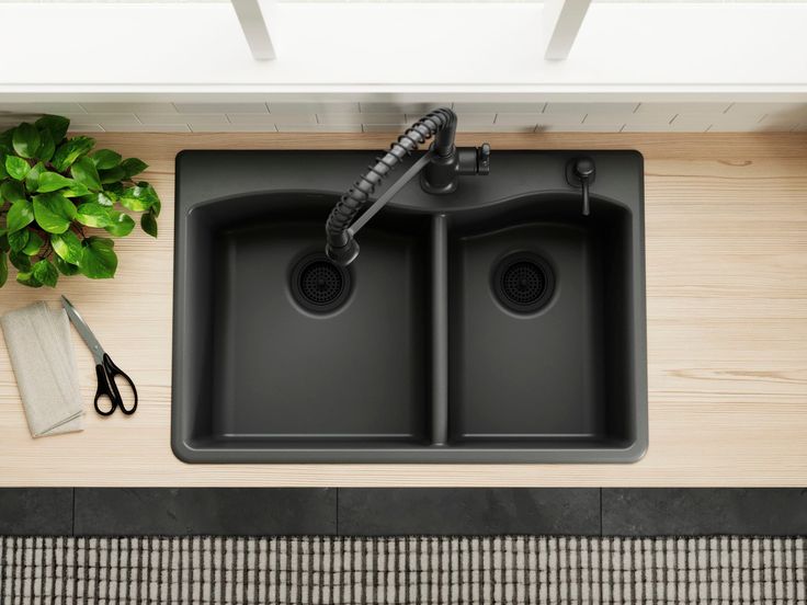 two black kitchen sinks sitting on top of a counter next to a potted plant