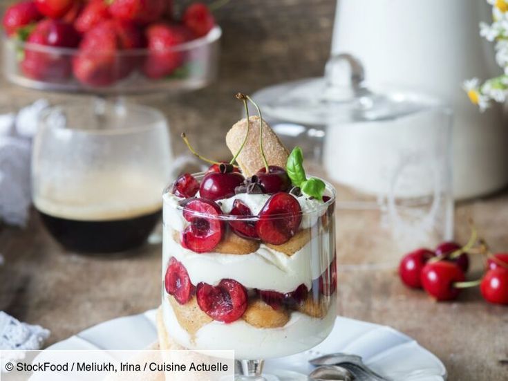 a dessert with cherries and whipped cream on a plate next to a pitcher of coffee