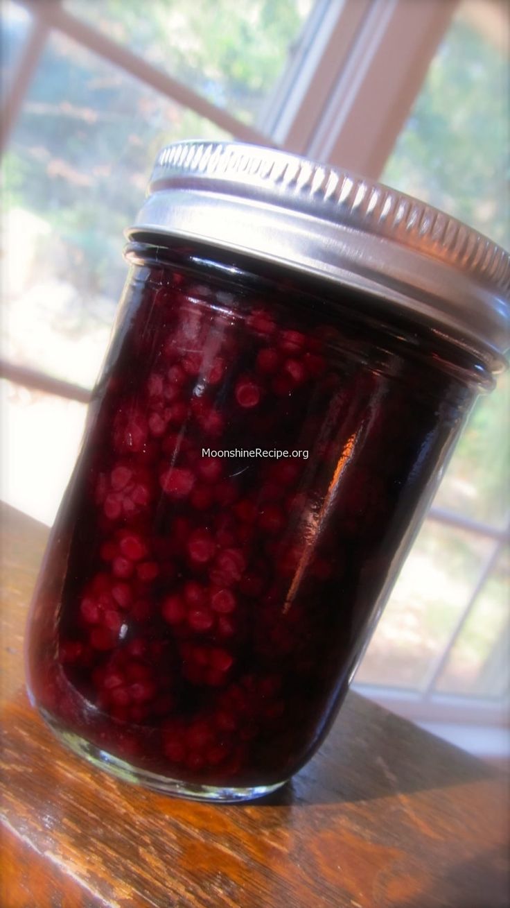 a jar filled with red liquid sitting on top of a wooden table next to a window