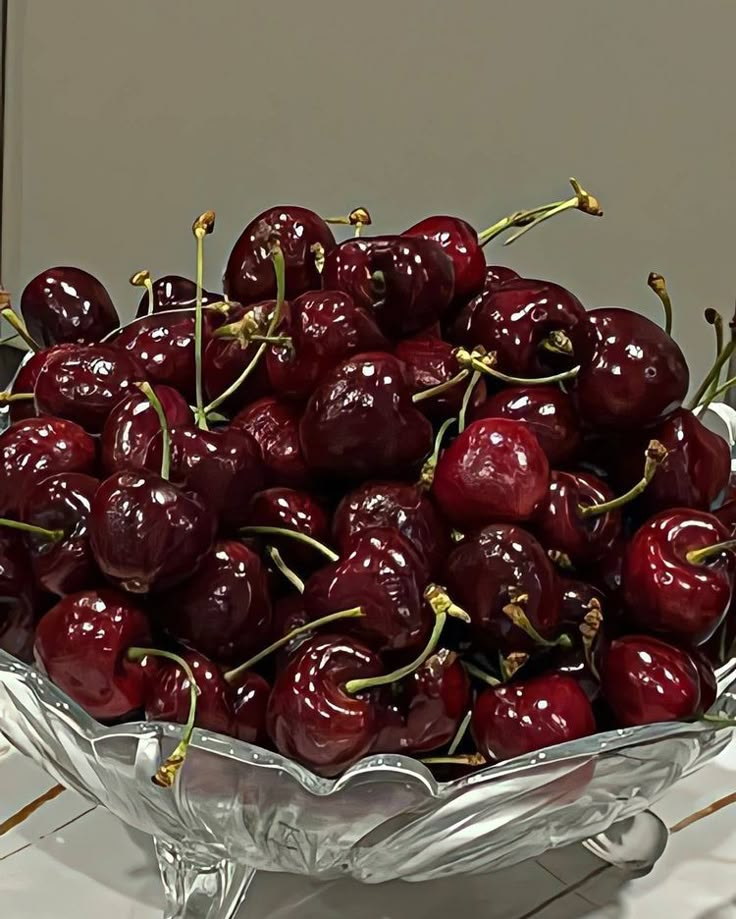 a glass bowl filled with lots of cherries on top of a white countertop