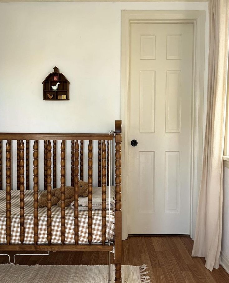 a wooden crib in front of a white door with a clock on the wall