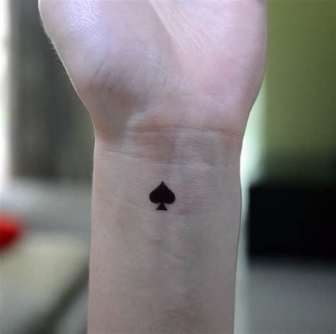 a small tattoo on the wrist of a person with a card suit in their left hand