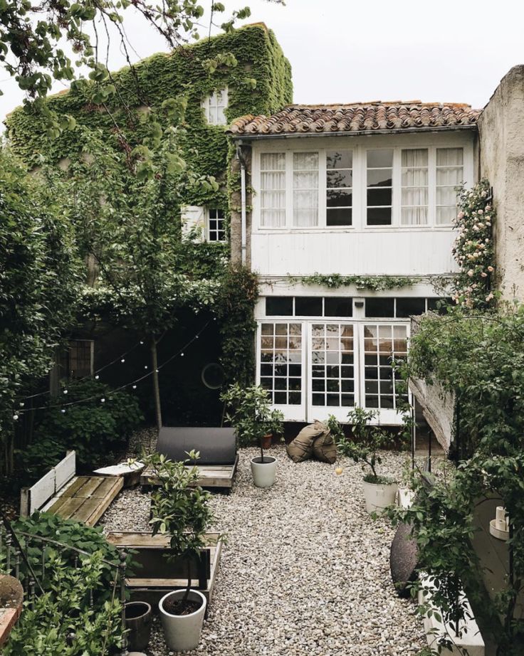 an old house is surrounded by greenery and potted plants on the gravel path