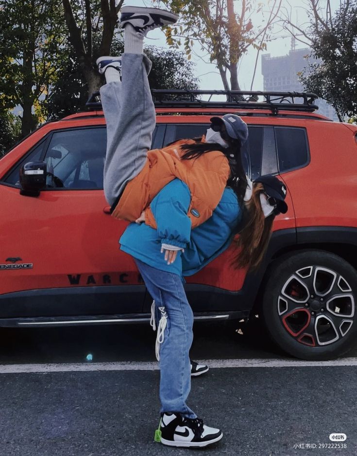 a person doing a handstand in front of a red car with the hood up