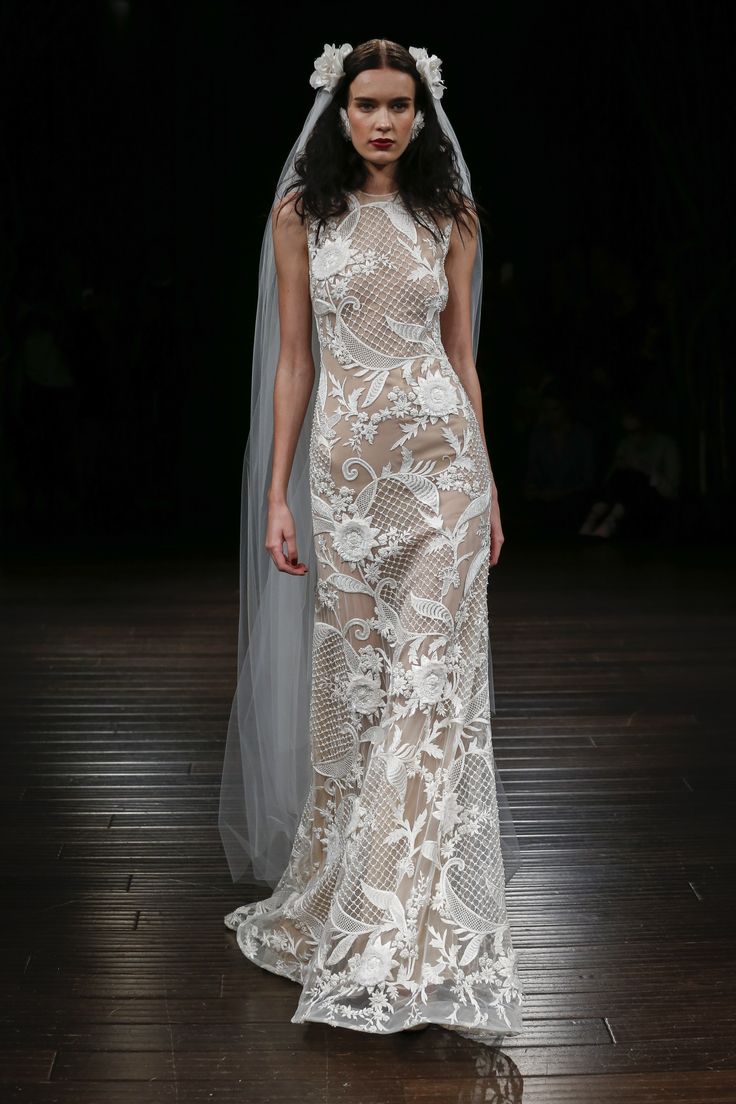 a model walks the runway in a white wedding dress with sheer veil and flowers on her head