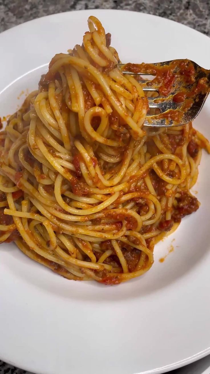 a white plate topped with spaghetti covered in sauce and a fork on top of it