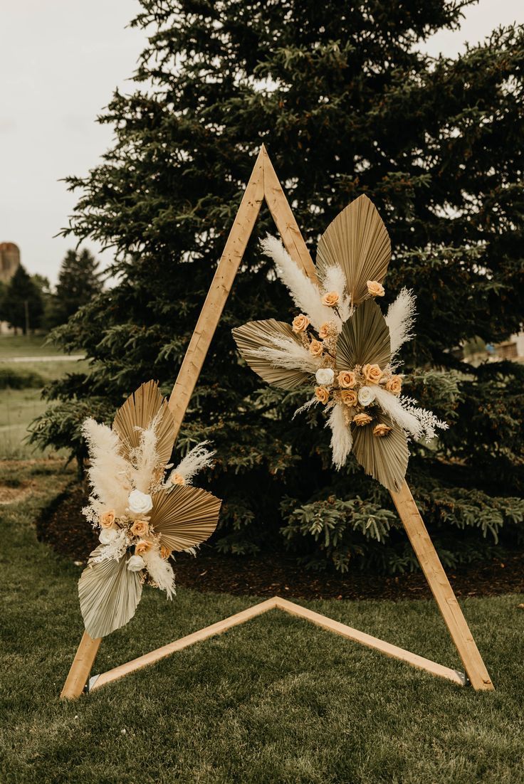 a wooden triangle with flowers and feathers on it sitting in the grass next to a tree