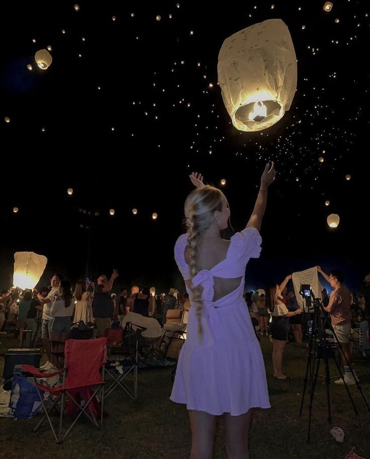 a woman in a white dress is releasing paper lanterns into the night sky with her hands